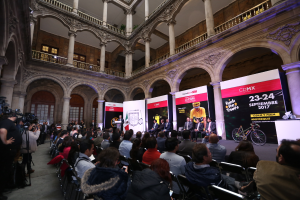 Eine Gruppe von Menschen, die an einem Tisch mit einem Podium und einem Mikrofon vor einer Menge, Kameras und Bannern sitzen, was eine Pressekonferenz für das CDMX 2017-Event suggeriert.