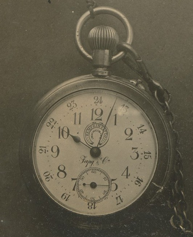 Ein Schwarz-Weiß-Foto einer alten Taschenuhr mit einer Kette, das eine nummerierte Zifferblätters zeigt.